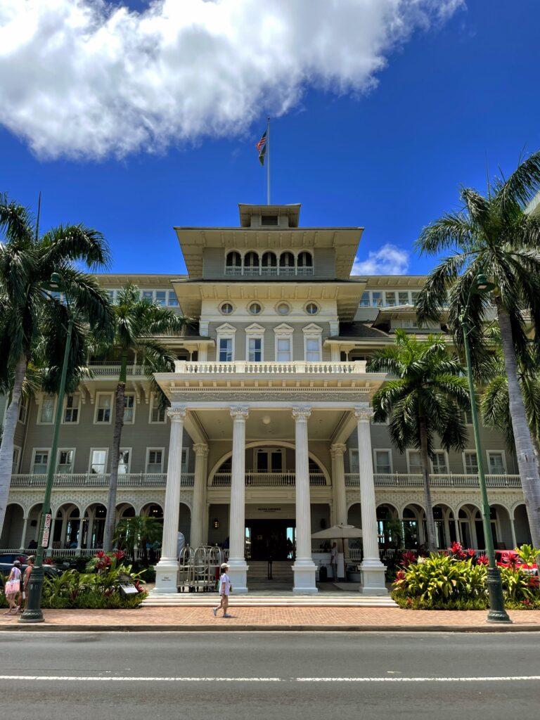 a large building with columns and a flag on top with Iolani Palace in the background