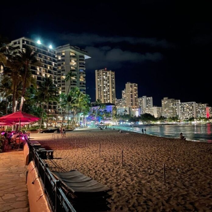 a beach with buildings and palm trees at night