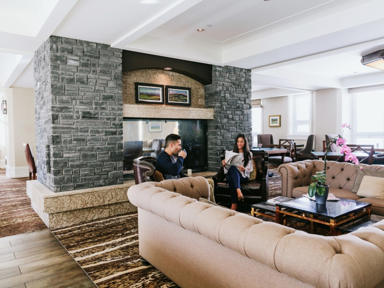 a man and woman sitting in a room with a fireplace and stone fireplace